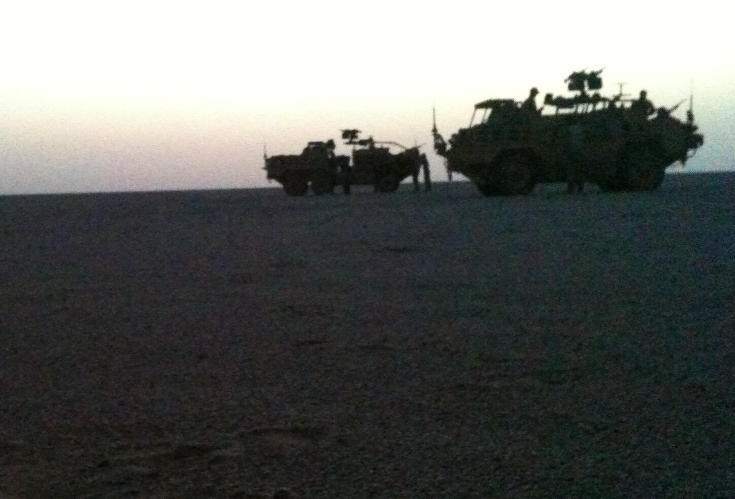 Military vehicles silhouetted against the horizon in a desert landscape at sunset.